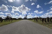 Militares formam em frente a igreja sob céu azul com nuvens
