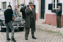 Equipa de filmagem em cena com ator vestido com fato clássico e carro antigo