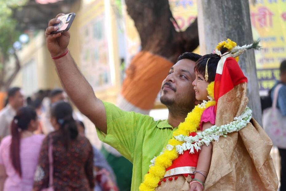 Menina indiana vestida como a deusa Durga ao colo do pai