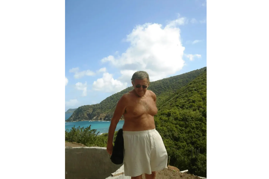 Homem sem camisa e calções desfruta da vista para o mar e a montanha