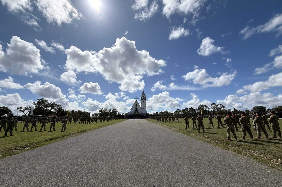 Militares formam em frente a igreja sob céu azul com nuvens