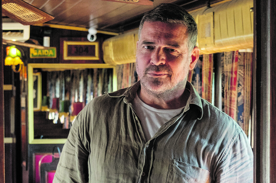 Homem pousa para foto num espaço interior com decoração clássica