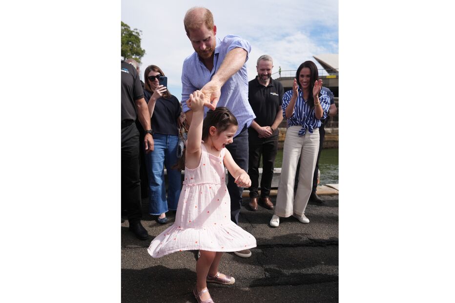 Harry dança com menina, sob o olhar atento de Meghan e outros populares