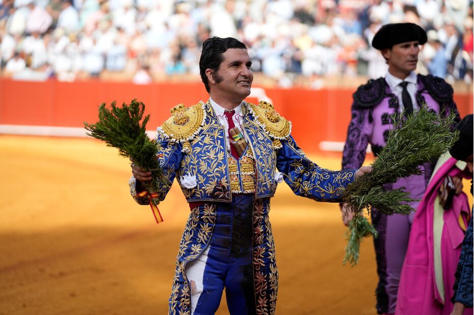 Um toureiro sorri, com ramos nas mãos, numa praça de touros