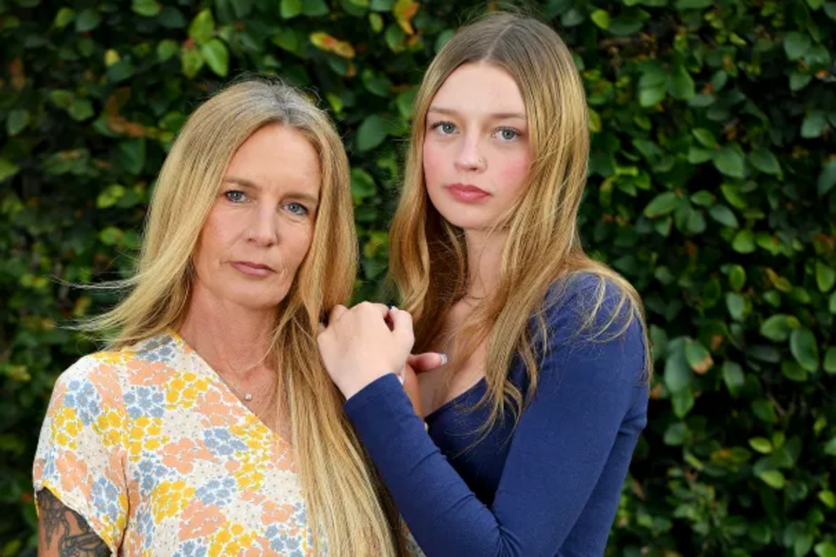 Mãe e filha posam juntas junto a um muro verde