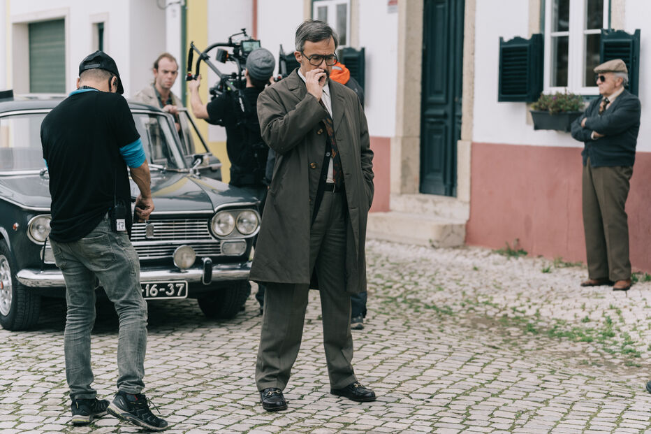 Equipa de filmagem em cena com ator vestido com fato clássico e carro antigo