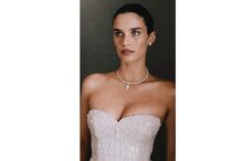 Mulher com vestido branco, colar e brincos a olhar para a esquerda