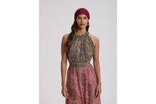 Mulher posa com vestido comprido e padrão paisley, e usa um gorro vermelho