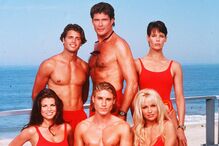 Elenco de Baywatch posa junto ao mar com fatos de banho vermelhos