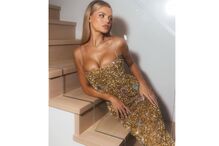 Mulher veste um vestido dourado brilhante com joias coloridas nas escadas
