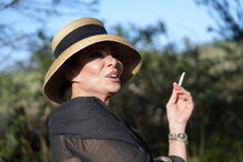 Mulher com chapéu de palha fuma cigarro com pulseiras douradas