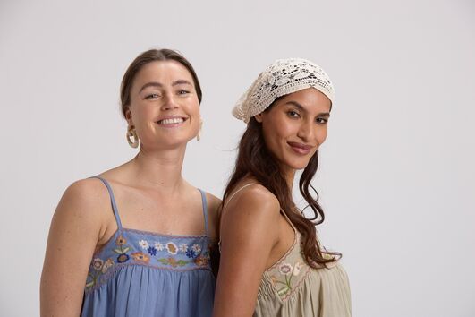 Mulheres sorrindo com vestidos bordados e touca de crochê