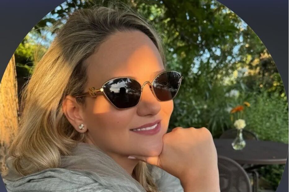 Mulher sorri com óculos de sol e pulseira dourada num ambiente verdejante