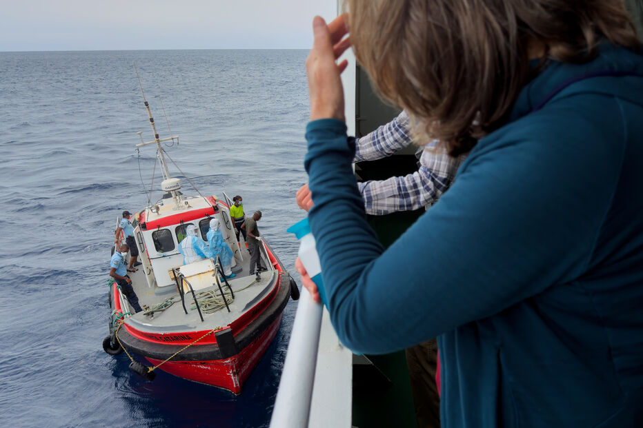 Os passageiros do navio de cruzeiro MV Hondius, afetado pelo hantavírus, observam os epidemiologistas a embarcarem no navio em Praia, durante a viagem com destino ao porto espanhol de Tenerife, a 6 de maio de 2026.
