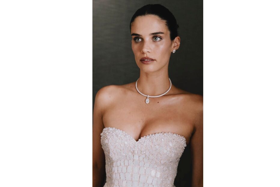 Mulher com vestido branco, colar e brincos a olhar para a esquerda
