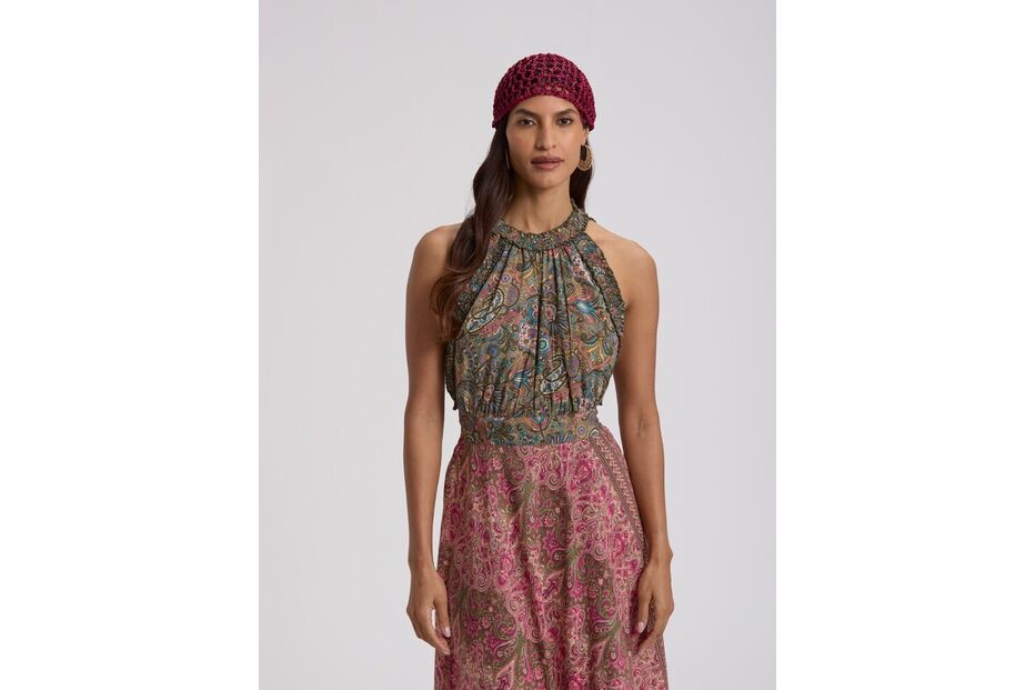 Mulher posa com vestido comprido e padrão paisley, e usa um gorro vermelho