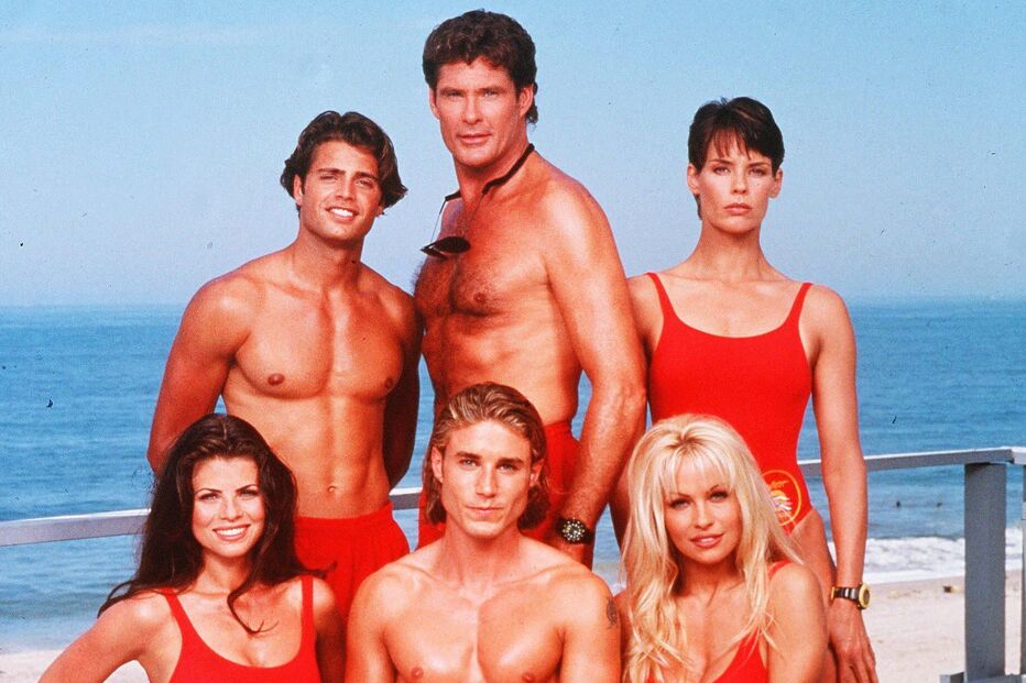 Elenco de Baywatch posa junto ao mar com fatos de banho vermelhos