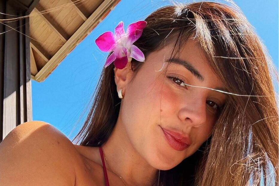 Mulher com flor no cabelo posa com céu azul e parte de edifício como fundo