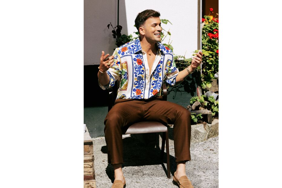Homem sorri com camisa estampada e calças castanhas, refletindo o percurso da vida