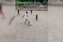 Vozinha descalço joga à bola com crianças num campo de terra batida em Cabo Verde