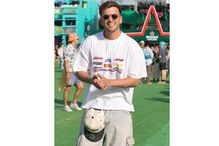 Um homem sorri com óculos de sol e t-shirt com logos, junto a um palco no festival NOS Alive