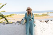Modelo com chapéu de palha e conjunto de calças e camisa azul turquesa, junto ao mar
