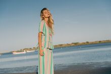 Mulher de cabelo loiro, de olhos fechados, usa um vestido às riscas coloridas numa praia