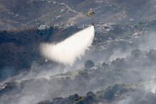 Um helicóptero combate um incêndio florestal numa área montanhosa perto de casas