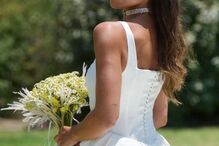Noiva com vestido branco e véu segura ramo de flores num jardim