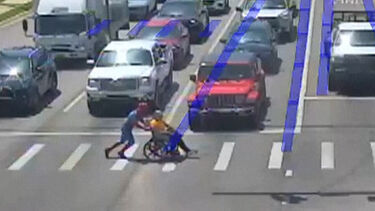 Homem vestido de Homem-Aranha ajuda pessoa em cadeira de rodas a atravessar a rua