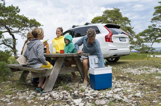 Família faz piquenique com carro estacionado junto à natureza