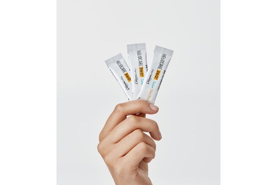 Mão segura 3 ampolas de Heliocare 360º Junior Oral Sticks