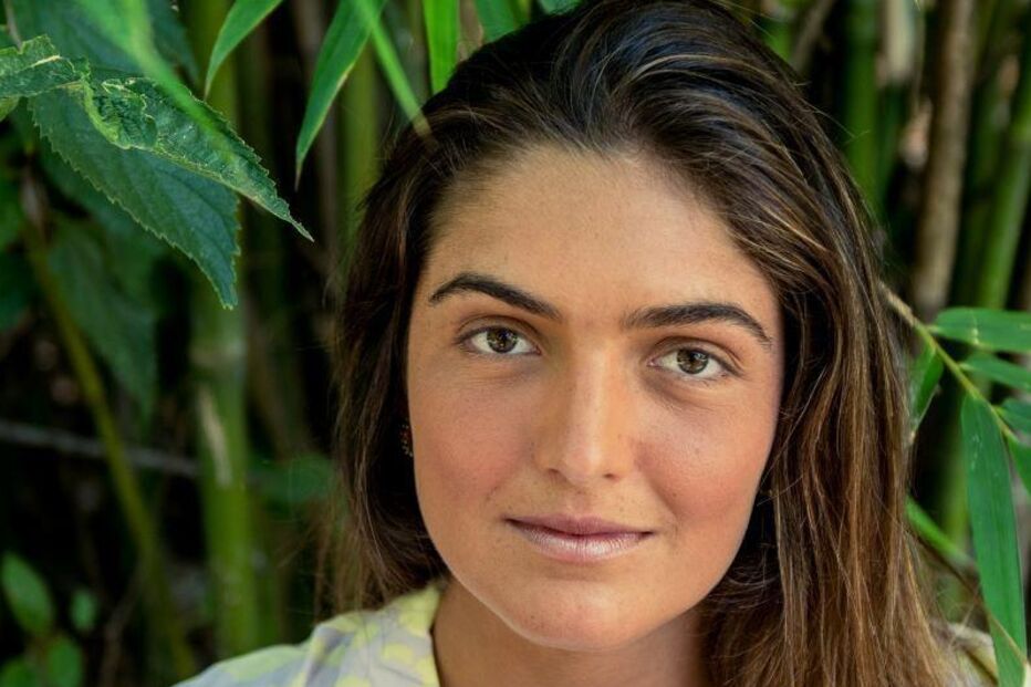 Mulher em frente a bambus, com uma camisa de padrão abstrato