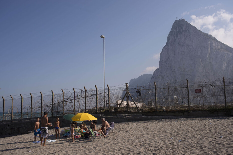 Pessoas na praia ao lado de uma cerca de separação entre Gibraltar, ao fundo, e Espanha, em La Línea de la Concepción