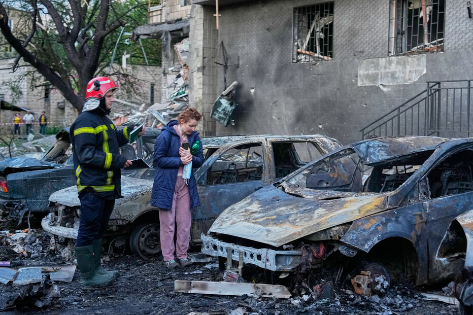 Bombeiro e civil em Kyiv junto a carros incendiados após ataque russo