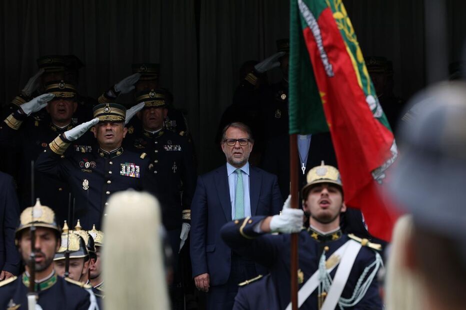 Homens uniformizados prestam continência a militar em parada com a bandeira de Portugal
