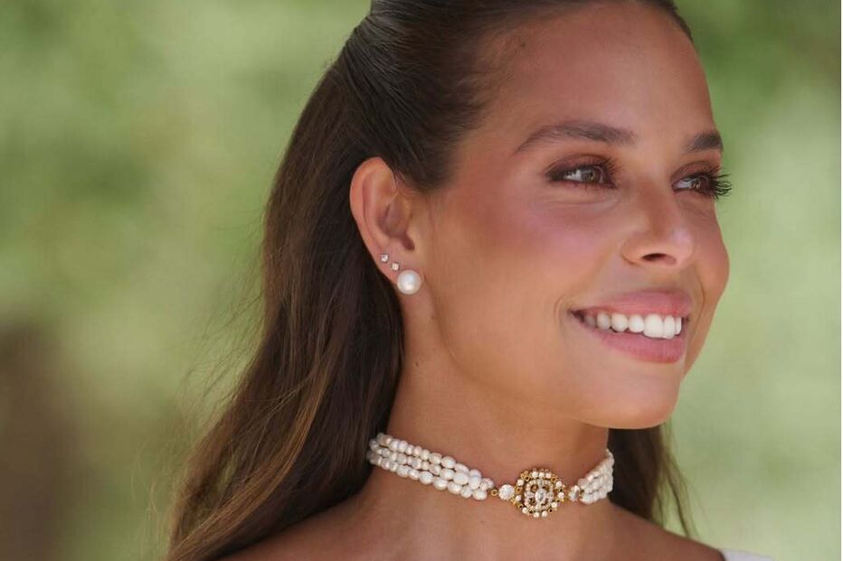 Mulher com colar de pérolas e brinco de pérola sorri para a câmara