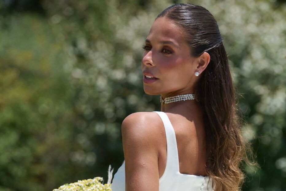 Noiva com vestido branco e véu segura ramo de flores num jardim