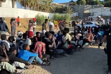Migrantes sentados em fila enquanto a polícia supervisiona em Ceuta