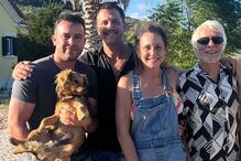 Pessoas e um cão posam em frente a uma casa num dia soalheiro