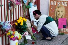 Um fã escreve uma mensagem a Dolly Parton ao lado de flores e um cartaz em homenagem