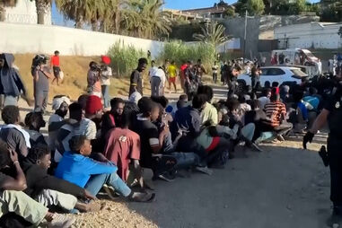 Migrantes sentados em fila enquanto a polícia supervisiona em Ceuta