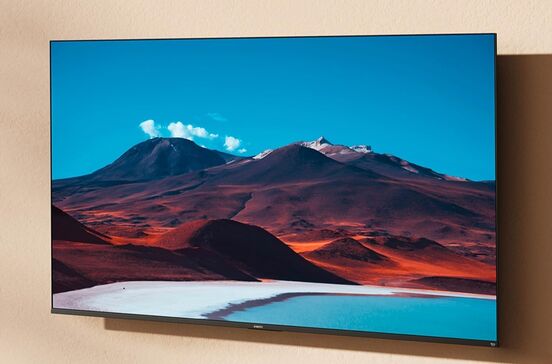 Televisão exibe paisagem com montanhas e lago azul sob céu claro