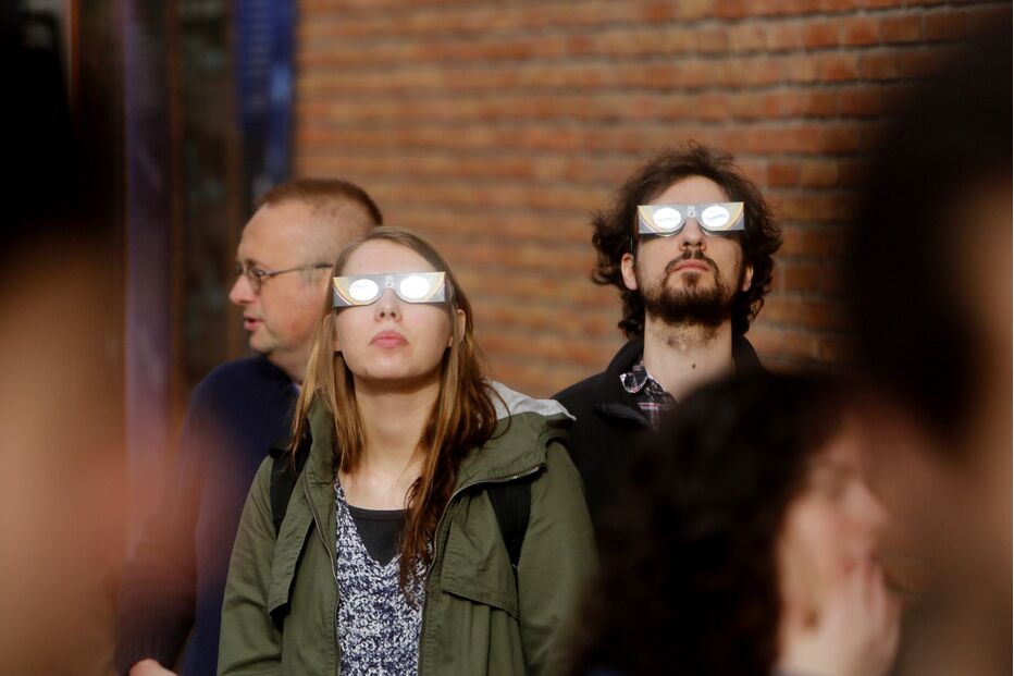 Pessoas observam eclipse solar com óculos especiais