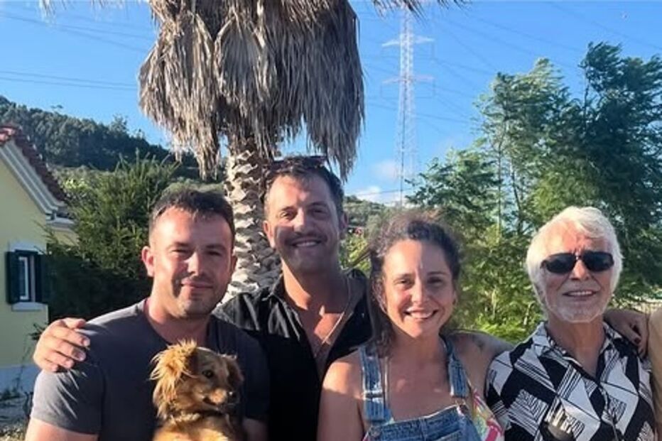 Pessoas e um cão posam em frente a uma casa num dia soalheiro