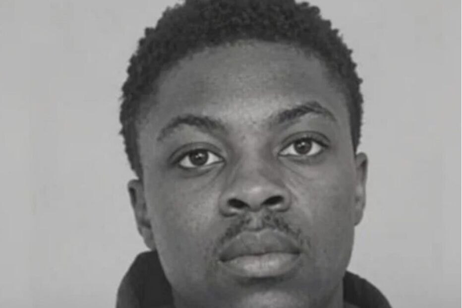 Um homem negro de cabelo curto e bigode encaracolado olha para a câmara