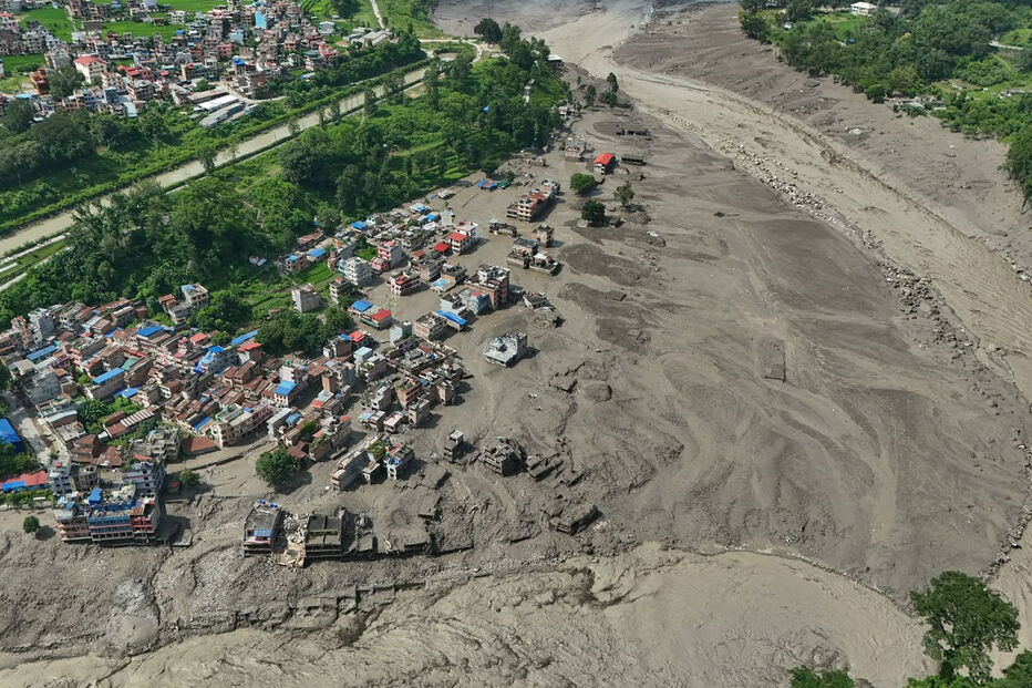 Damaged houses stand precariously near the swollen, debris-choked banks of the Trishuli River after flash floods in Nepal's Nuwakot district