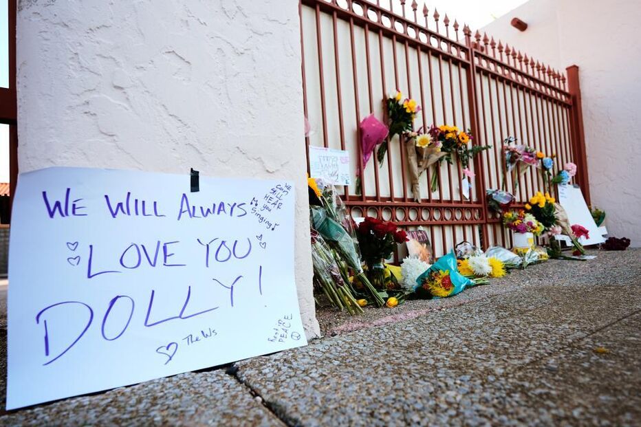 Um memorial com flores para Dolly Parton em frente a um portão com a mensagem 
