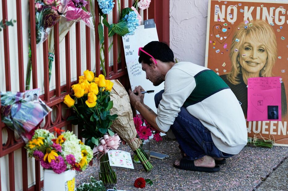 Um fã escreve uma mensagem a Dolly Parton ao lado de flores e um cartaz em homenagem