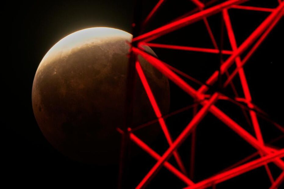 A partial lunar eclipse is seen beyond a television tower